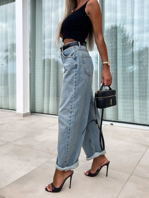 Baggy light wash denim barrel leg jeans with cuffed hems, styled with a black top and heels.