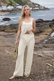 Open-knit crochet tank and wide-leg trouser set in beige, styled with a straw bag.