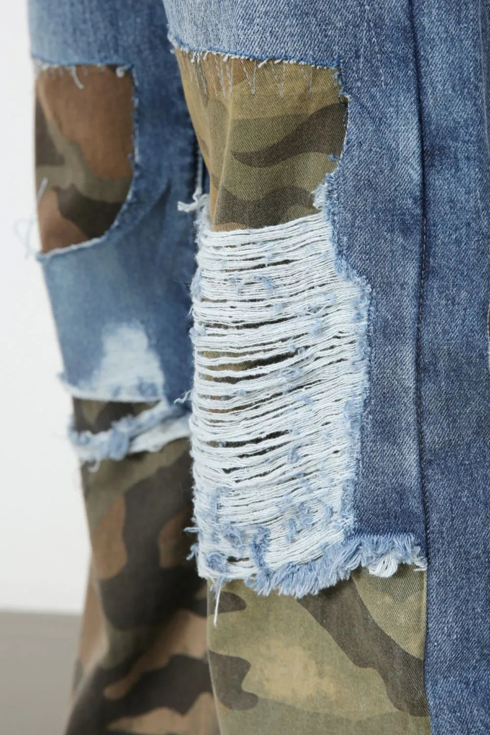 Camouflage patchwork distressed jeans in medium wash denim with frayed rips and camo print panels.