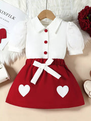 Red baby skirt with white heart appliques and white puff sleeve top with red buttons.