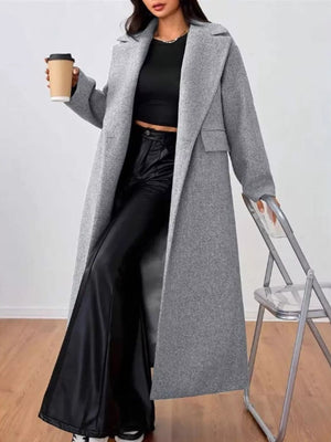 Gray wool-blend longline overcoat with notch lapels and flap pockets, worn open over black pants.