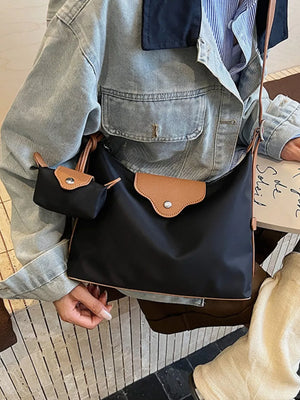 Black canvas hobo bag with coin purse and tan trim, worn casually.