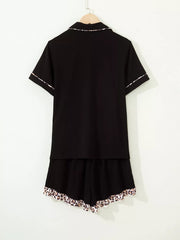 Black button-up pajama set with short sleeves and leopard trim on collar, cuffs, and shorts.