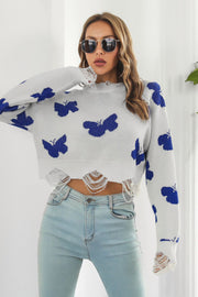 White acrylic cropped sweater with blue butterfly intarsia and frayed hem detail.