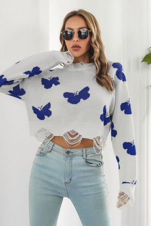White acrylic cropped sweater with blue butterfly intarsia and frayed hem detail.