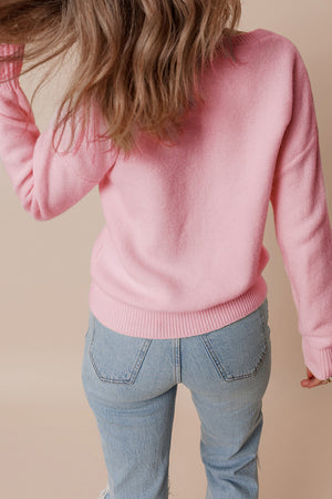 Blush pink knit sweater with floral appliqué detail and ribbed cuffs and hem.