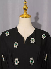 Black midi dress with puff sleeves and scattered rhinestone and emerald embellishments.