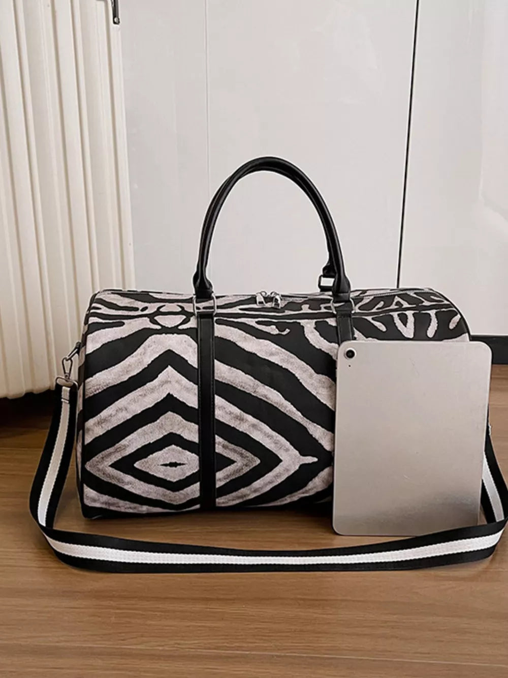 Bold zebra print duffle bag with black carry handles and detachable strap.