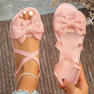 Pink crisscross bow sandals with ankle straps and a textured bow detail.