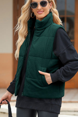 Dark green corduroy padded vest with a high collar and zip front, styled over a black hoodie.