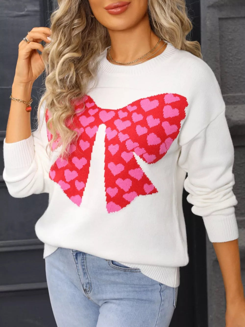 White knit sweater with a red and pink heart bow graphic, round neck, long sleeves.