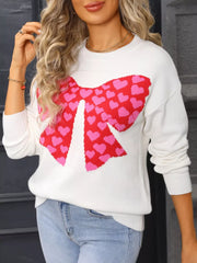 White knit sweater with a red and pink heart bow graphic, round neck, long sleeves.