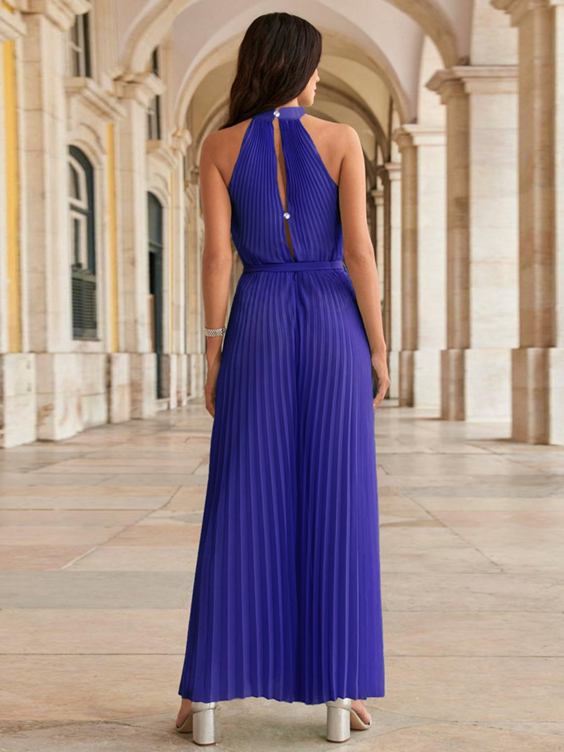 Pleated palazzo jumpsuit in royal blue with halter neckline and back cutout detail.