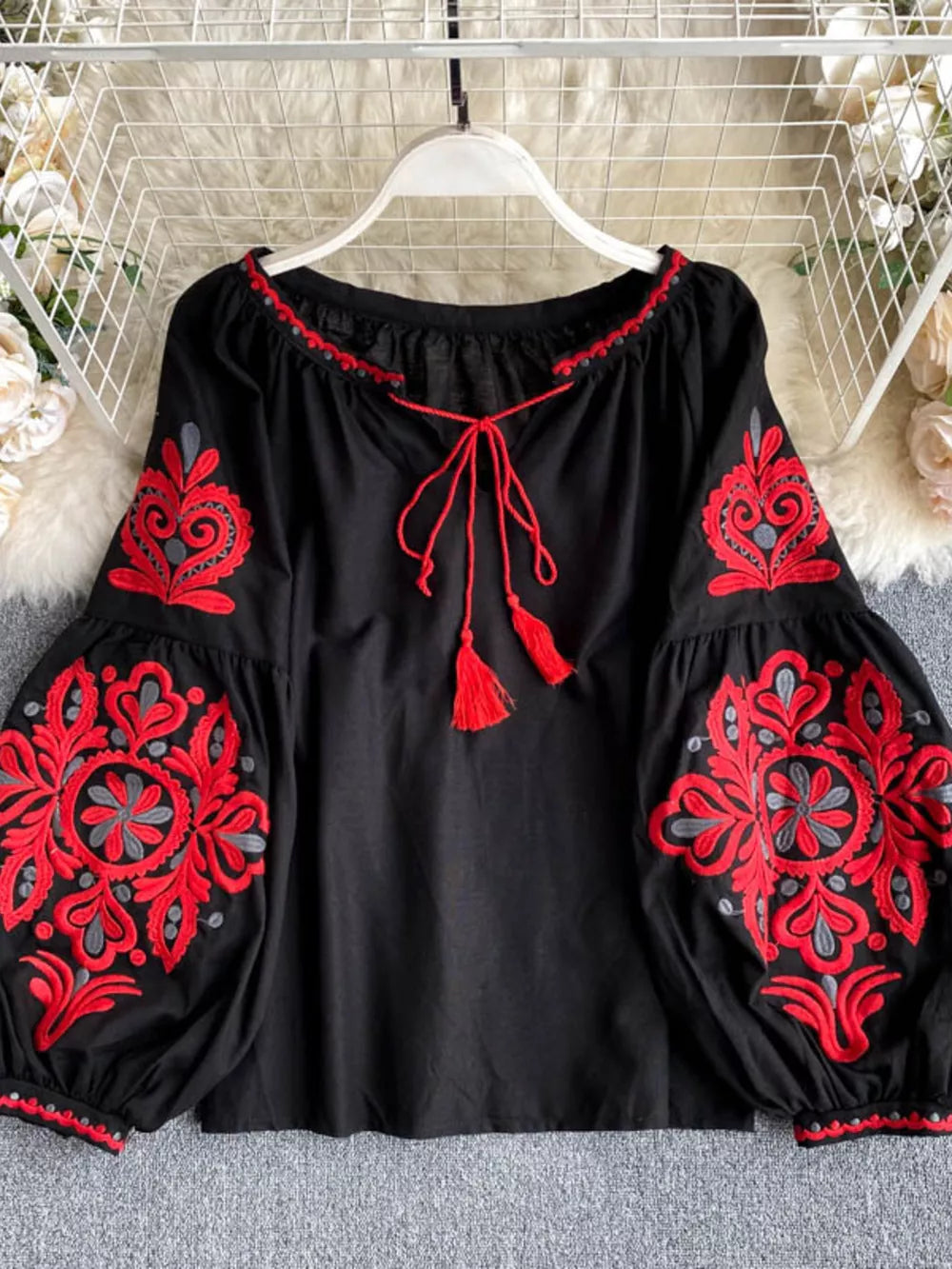 Black peasant blouse with red embroidery, tie neck, and tassel details.