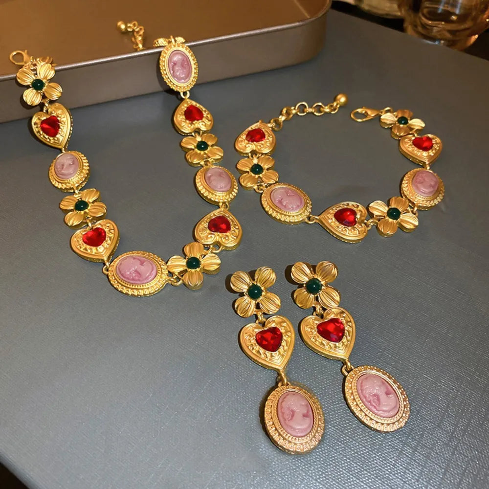Gold cameo and floral statement necklace with red heart and green gem accents.