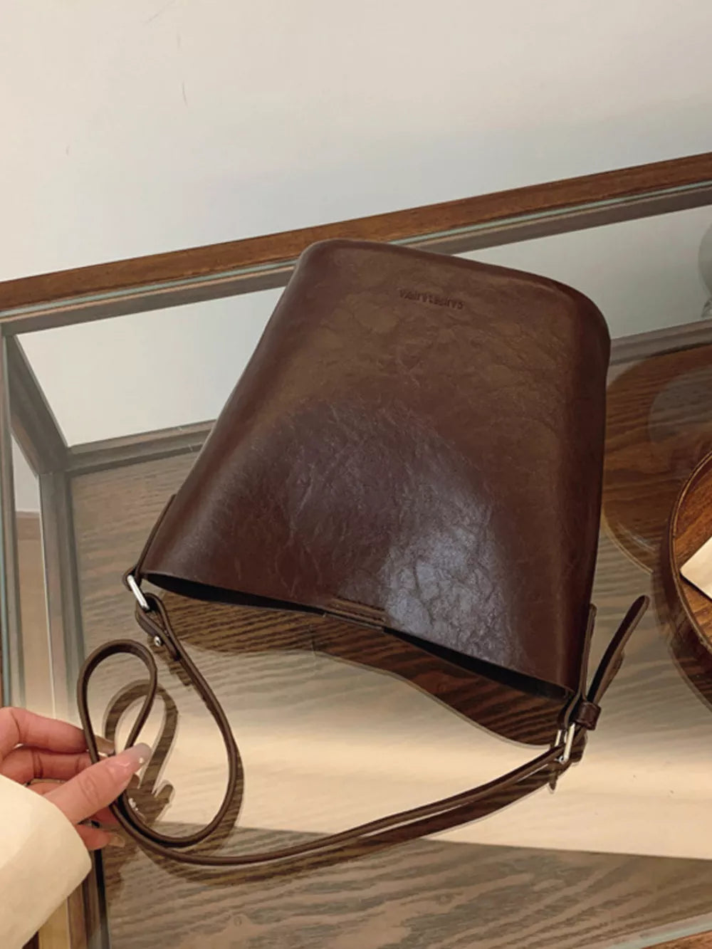 Distressed vintage bucket crossbody bag in brown with adjustable strap and embossed logo detail.
