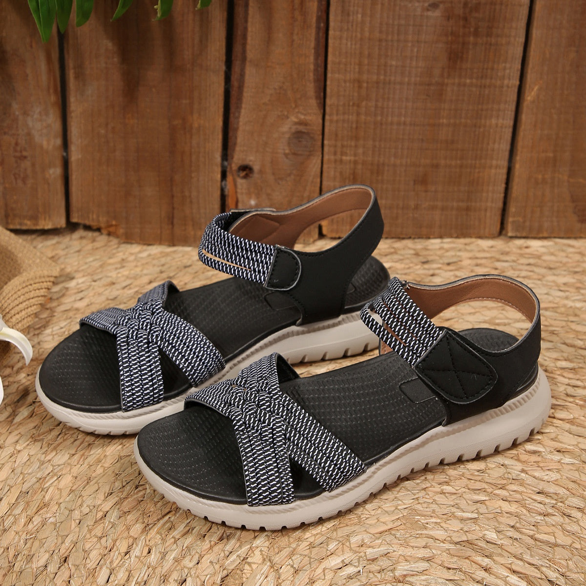 Black woven strap open-toe flat sandals with adjustable velcro closure.
