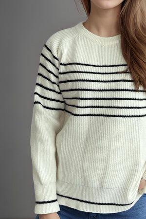 White ribbed knit crewneck sweater with black breton stripes and crew neckline.