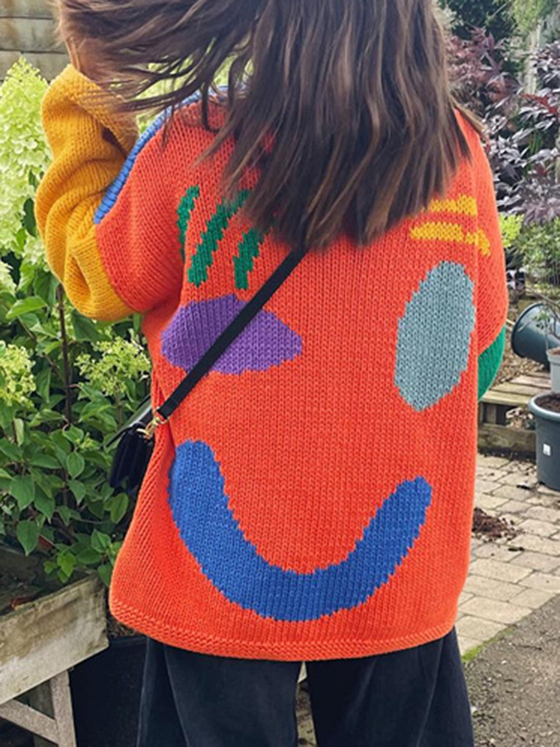 Orange knit sweater with abstract graphic pattern and smiley face detail.