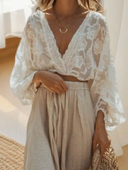 Elegant white lace crop top with deep V-neck and flowing sleeves, paired with a beige linen skirt.