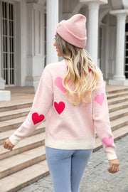 Blush pink intarsia knit crewneck sweater with red and pink hearts, cream trim, and long sleeves.