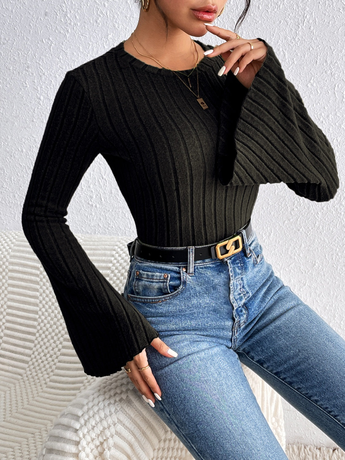 Black ribbed sweater with flared sleeves and crew neck, styled with jeans.
