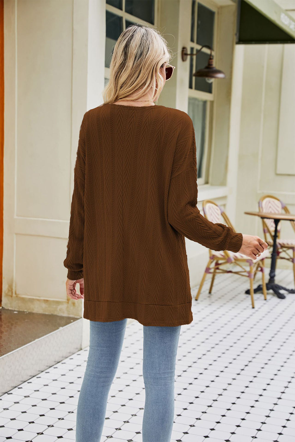 Chestnut cable-knit cardigan with chevron pattern and pockets, worn casually with jeans.