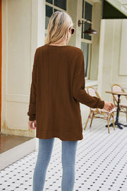 Chestnut cable-knit cardigan with chevron pattern and pockets, worn casually with jeans.