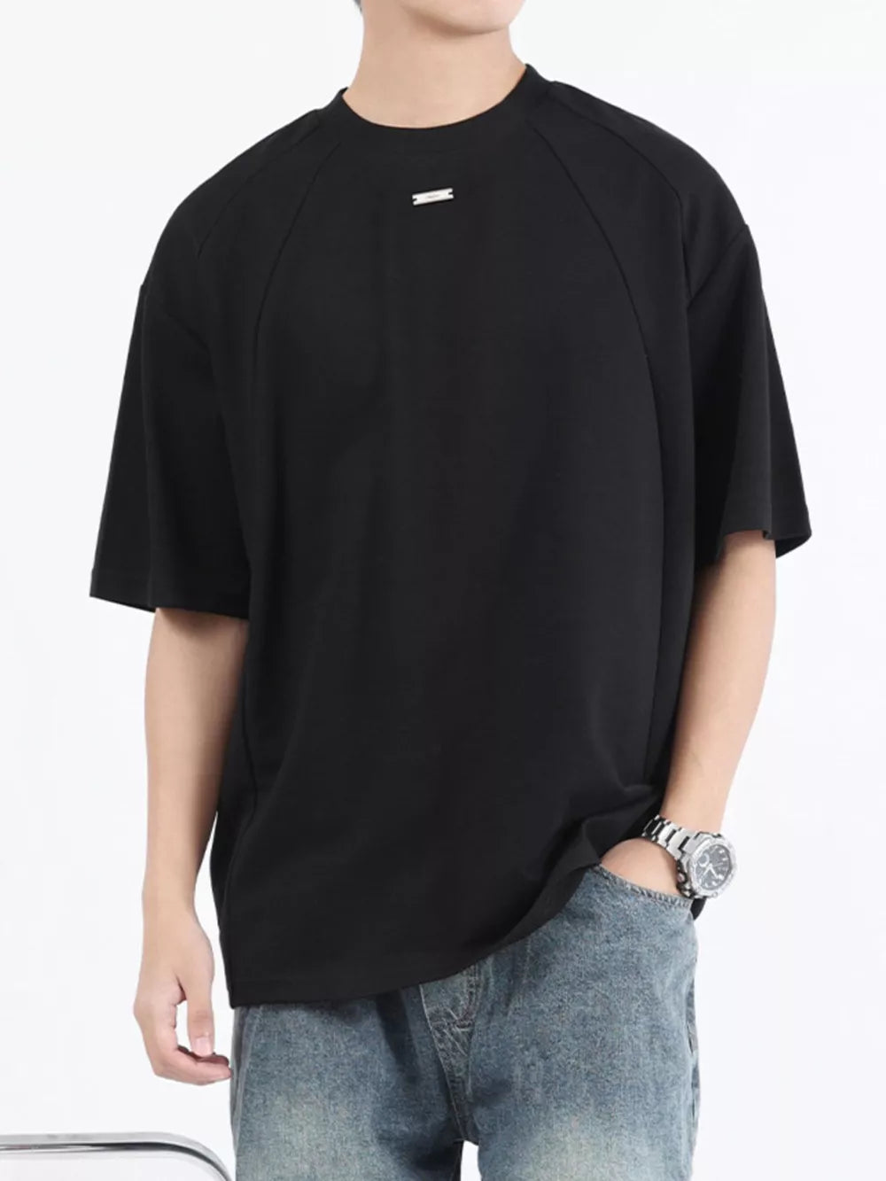 Black cotton t-shirt with round neck and short sleeves, featuring subtle seam details and a small metallic accent.
