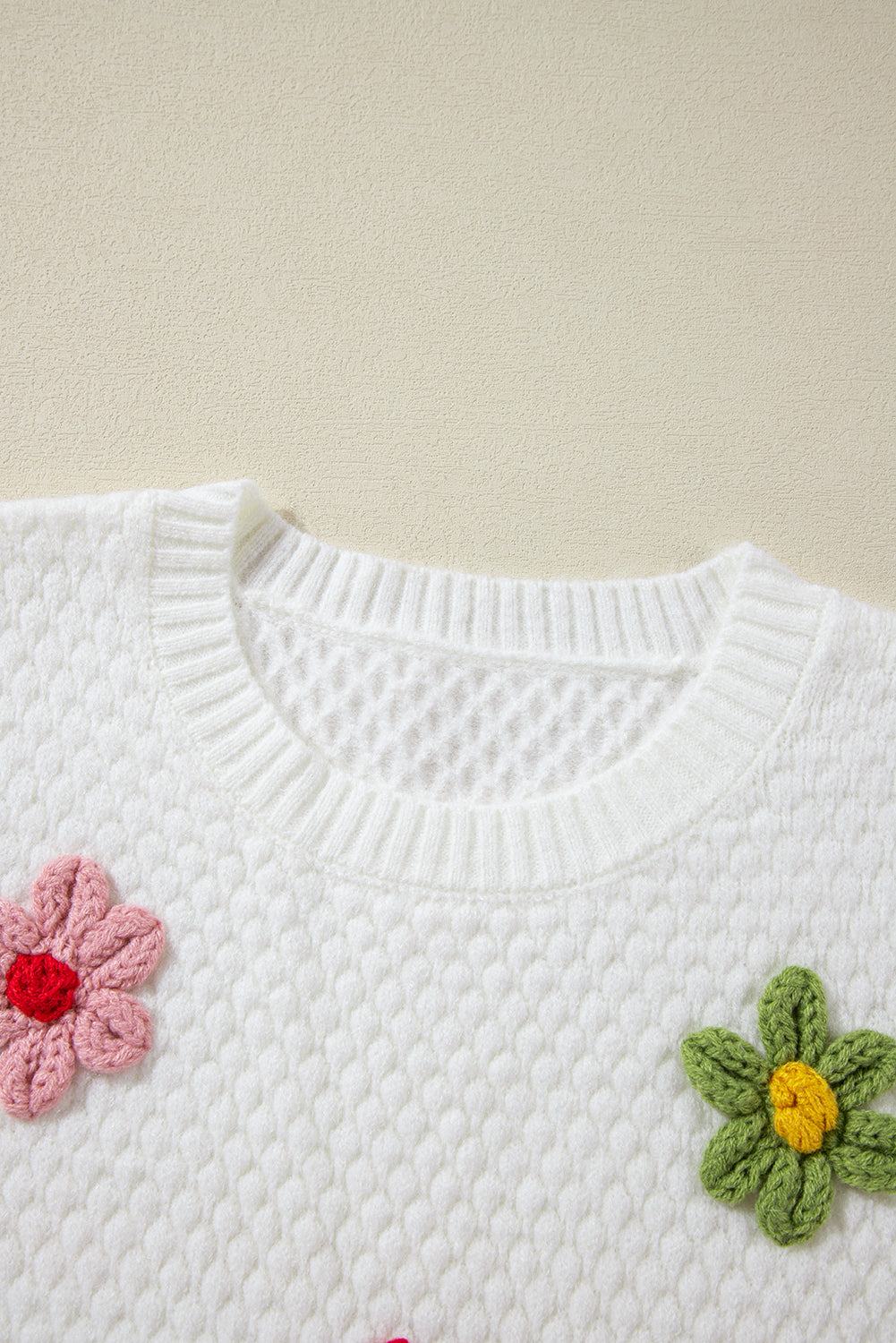 White knit sweater with crochet floral embellishments and a crew neck.