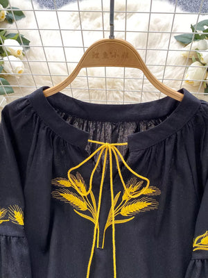 Black tie-neck blouse with yellow wheat embroidery and ruffled sleeves.