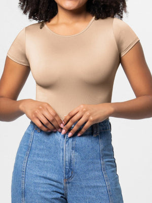 Tan scoop-neck bodysuit with short sleeves, smooth fabric, worn with jeans.