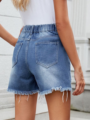 Medium wash denim shorts with elastic waist, frayed hem, and asymmetric shredding detail.