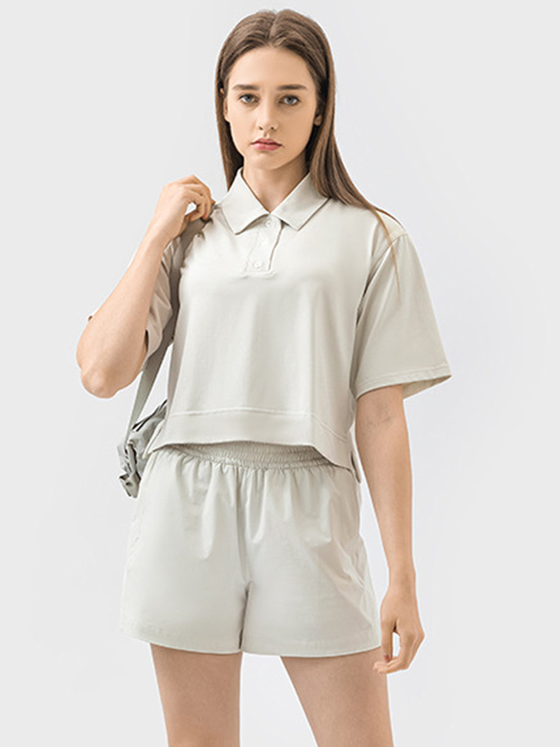 Cropped beige polo top with short sleeves and a button placket, styled with matching shorts.