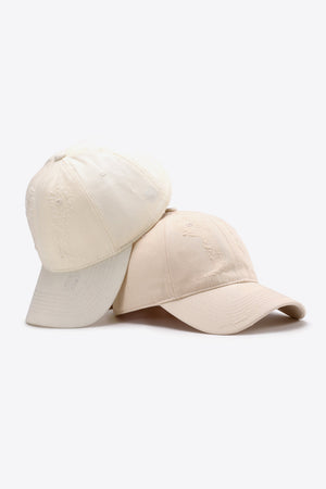 Two distressed baseball caps in cream and off-white with embroidered details.