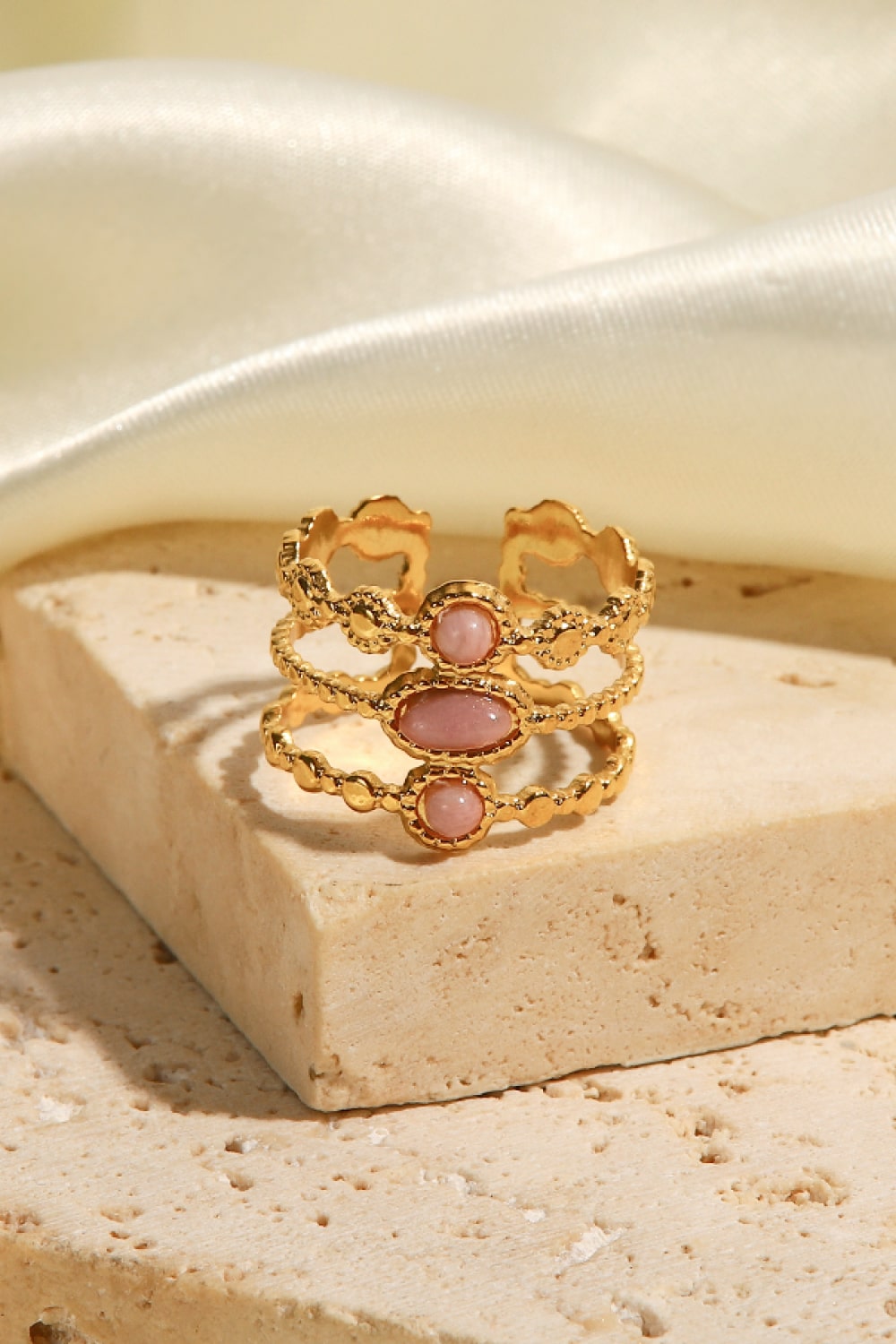 Gold triple stone openwork ring with pink stones and textured bands.