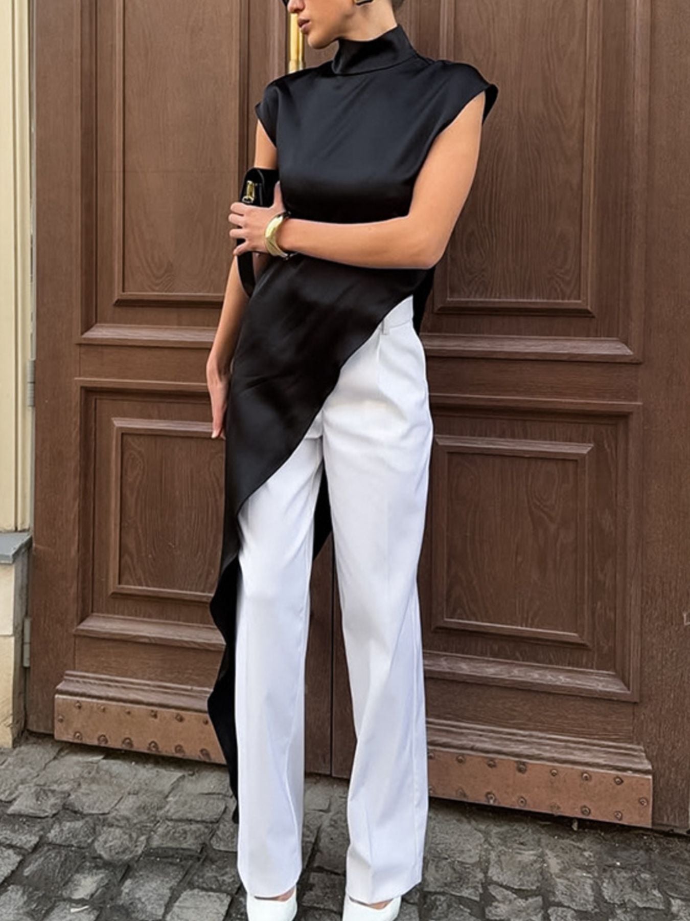 Black asymmetrical hem turtleneck blouse with cap sleeves and draped detail.