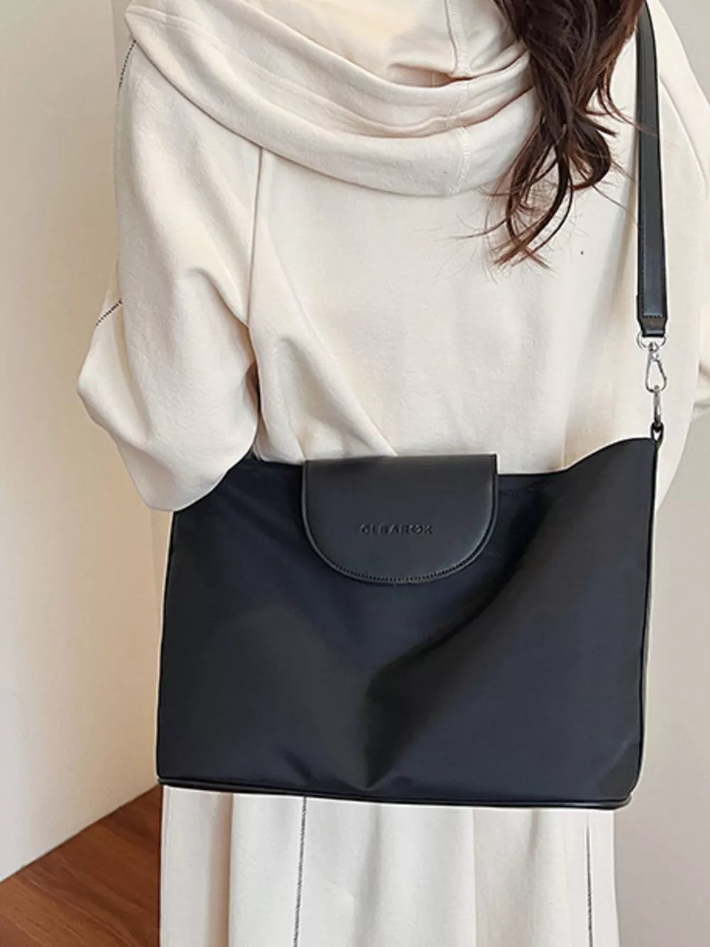 Black canvas hobo crossbody bag with a flap closure and embossed logo detail.
