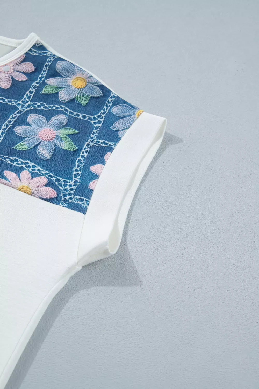 White t-shirt with embroidered floral detail on blue denim-look fabric and cuffed sleeves.