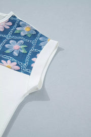 White t-shirt with embroidered floral detail on blue denim-look fabric and cuffed sleeves.