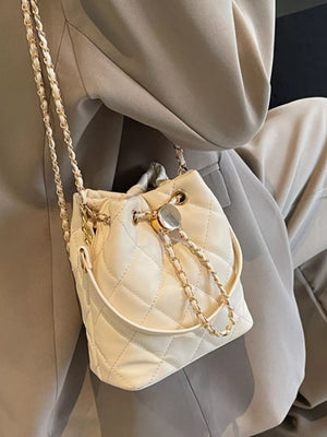 White quilted bucket crossbody bag with gold chain strap and drawstring closure.
