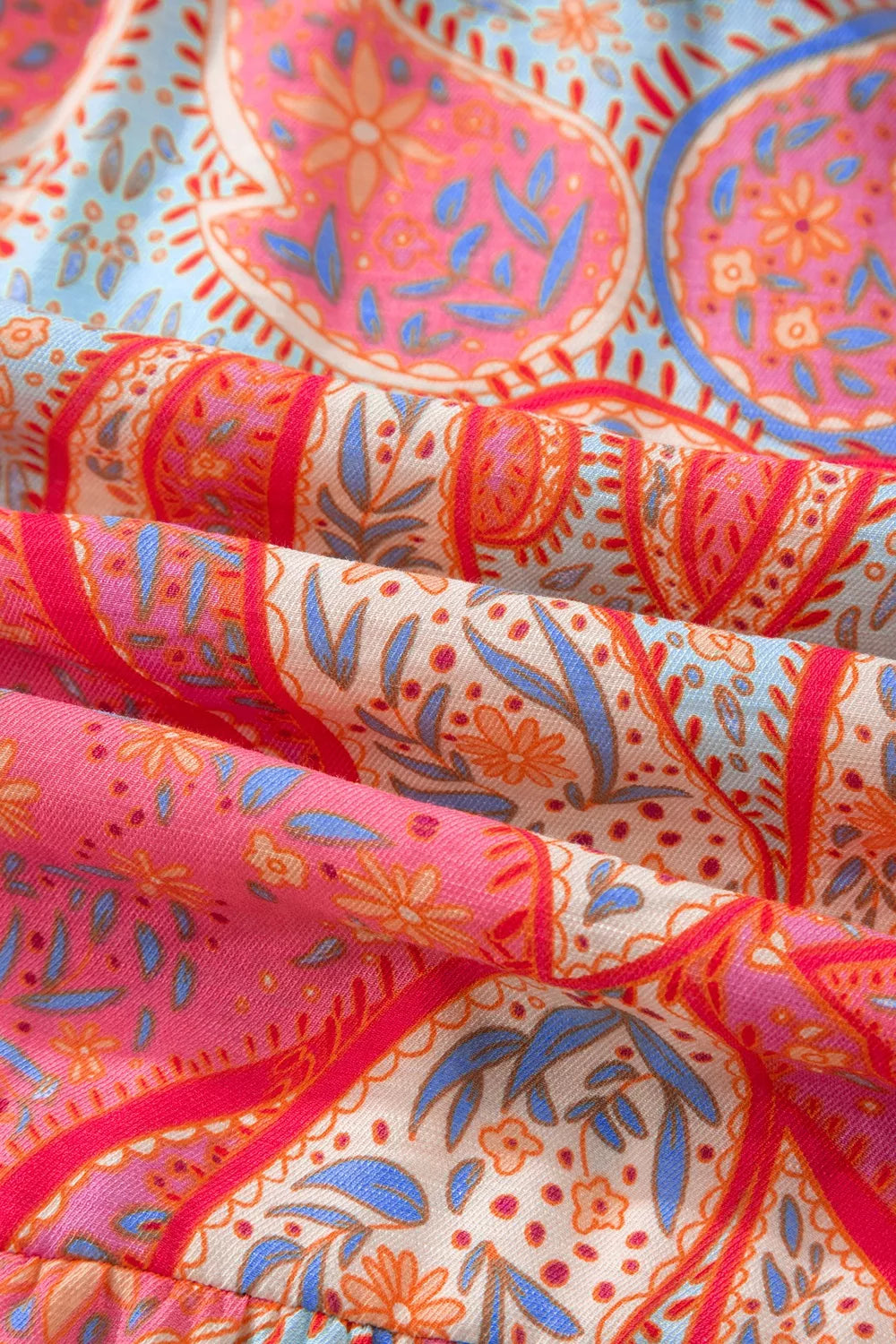 Paisley print boho dress fabric detail in coral pink with blue and orange floral accents.