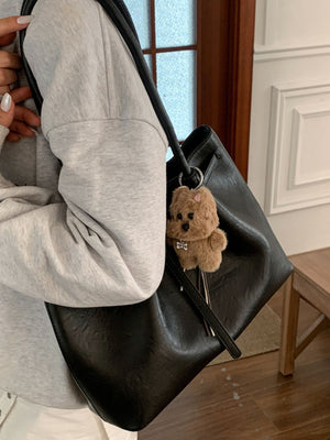 Black leather shoulder bag with buckle detail and a fluffy dog charm.