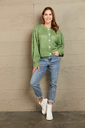 Green acrylic cropped cardigan with bubble sleeves and button front, styled with jeans.