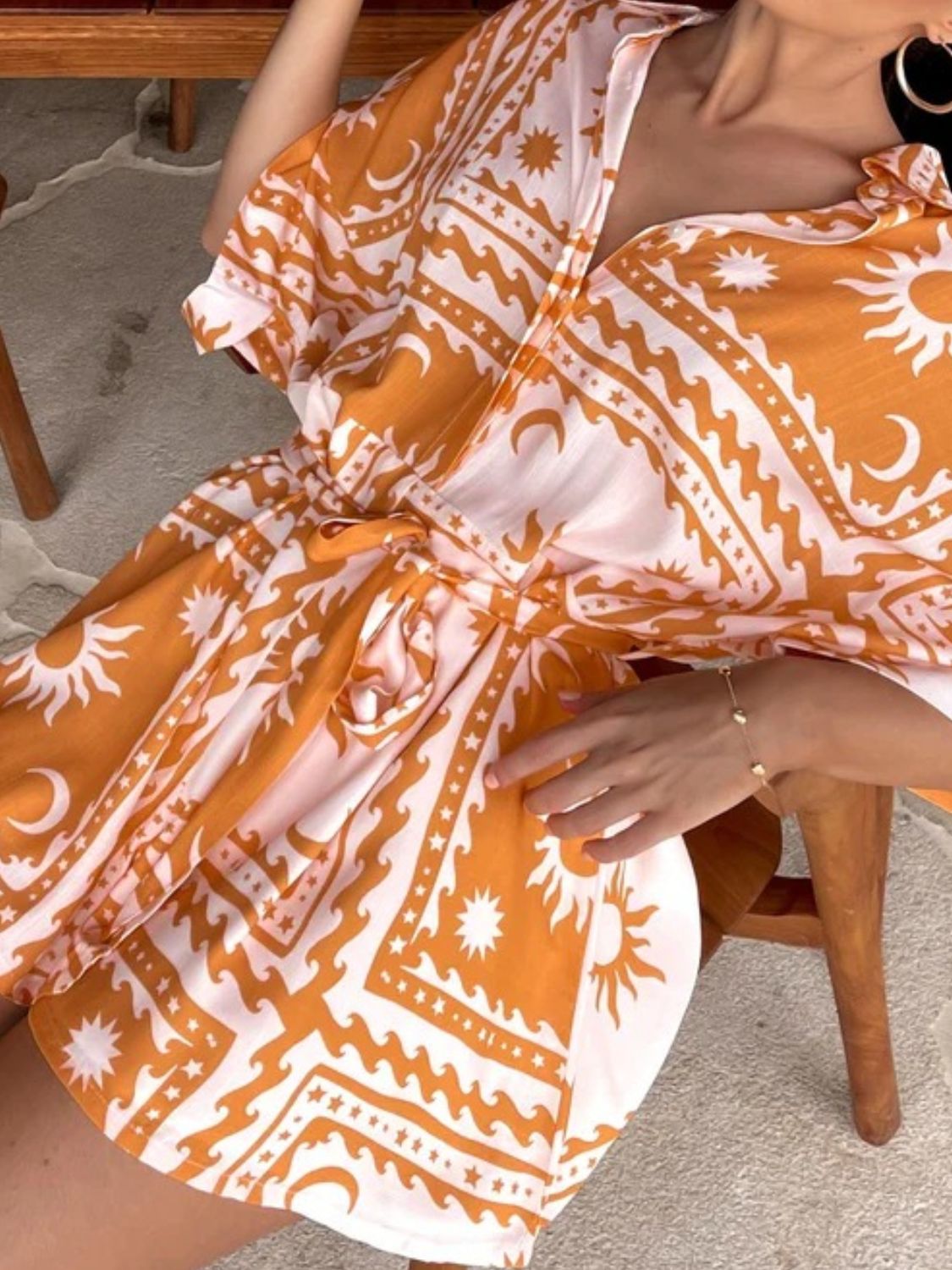 Wrap romper with celestial print in orange and white, featuring a V-neck and tie waist.