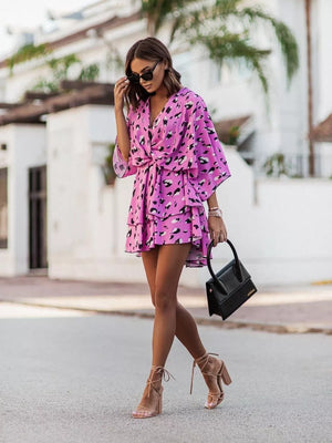 Tropical tiered mini dress in fuchsia pink with a leopard print, surplice neckline, and belted waist.