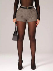 Chic houndstooth high-waisted shorts with a belted waist, styled with sheer top and black heels.