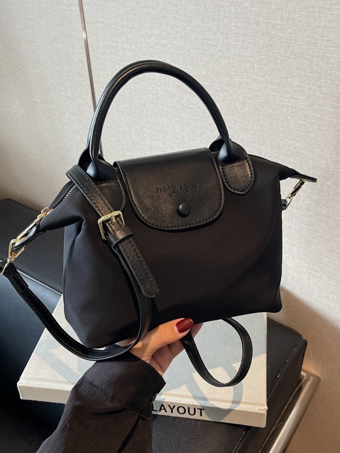 Black nylon crossbody bag with leather flap and top handle, adjustable strap.