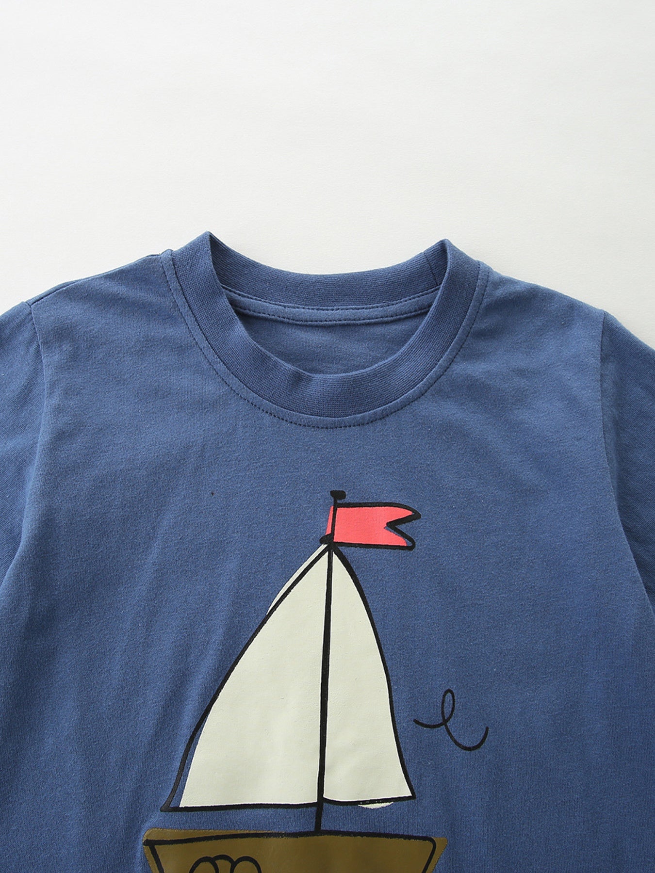 Blue cotton tee with sailboat graphic and red flag detail.