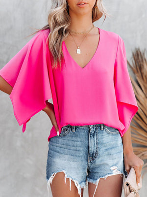 Chic V-neck blouse with flutter sleeves in bright pink, styled with denim shorts.